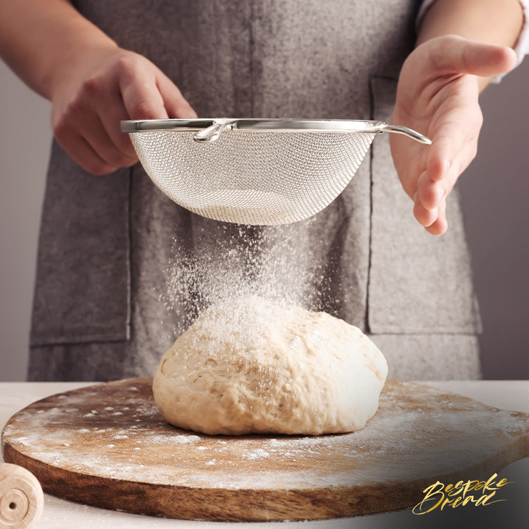 Baker sifting flour over sourdough on a table