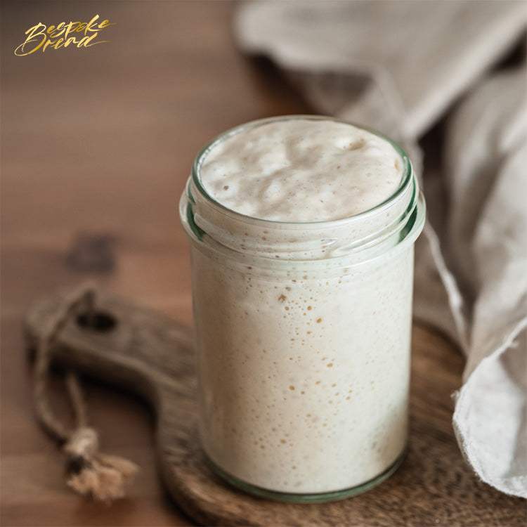 hands mixing flour and water to make sourdough starter in a glass bowl