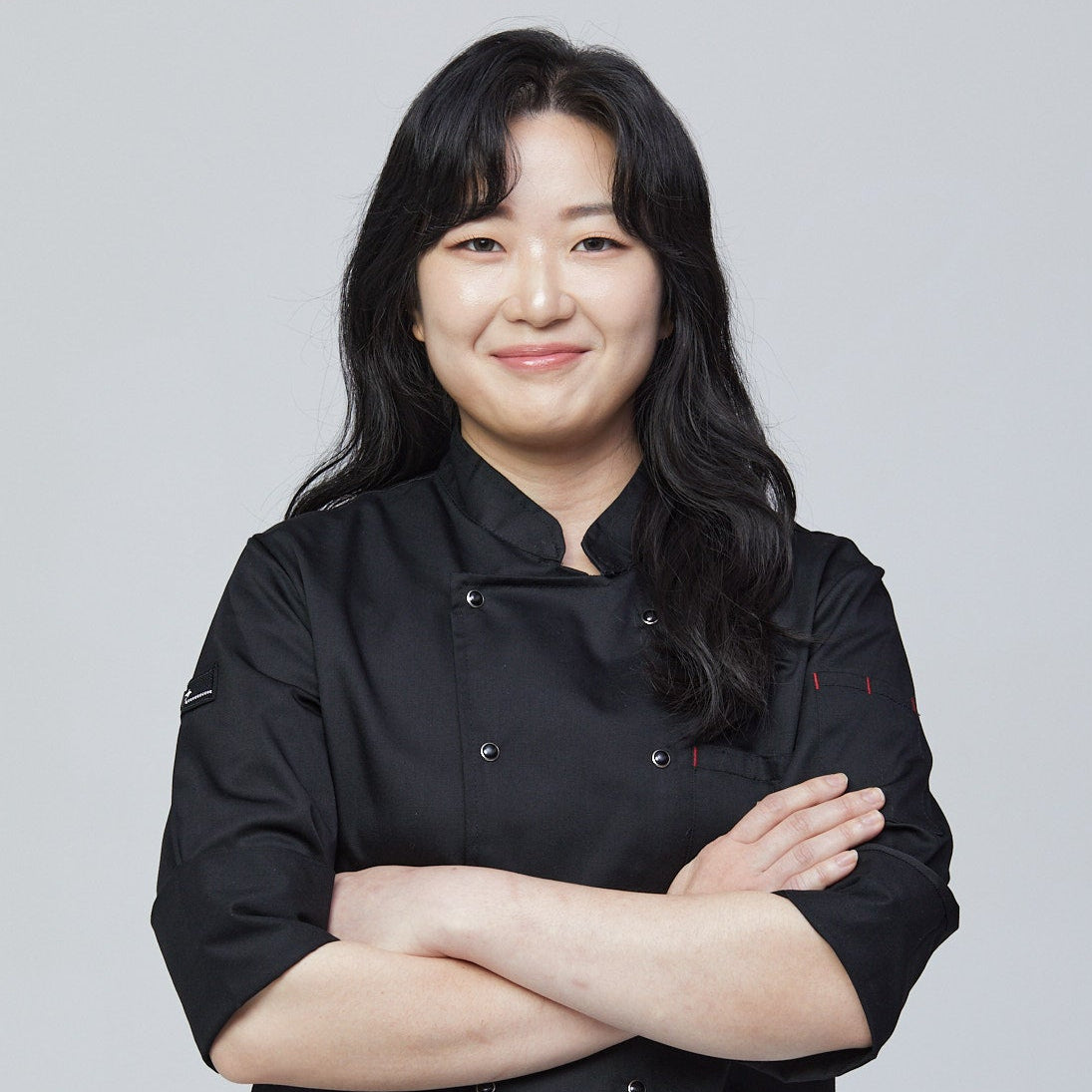 Person wearing a black chef's coat against a gray background